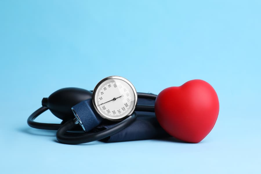 Blood pressure meter with toy heart on light blue background
