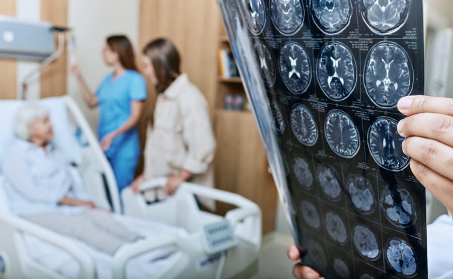 Patient laying in hospital bed while physician looks at images of brain scan