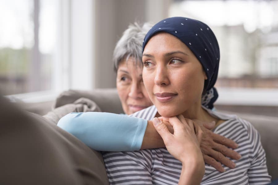 Breast cancer patient wearing headscarf in foreground clutching family member’s arm