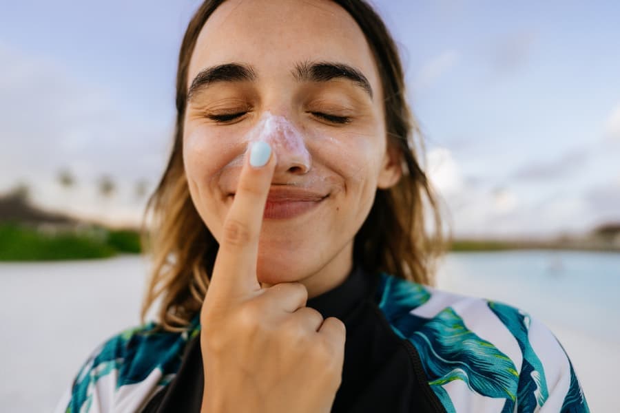 Young person applying sunscreen on nose to prevent skin cancer