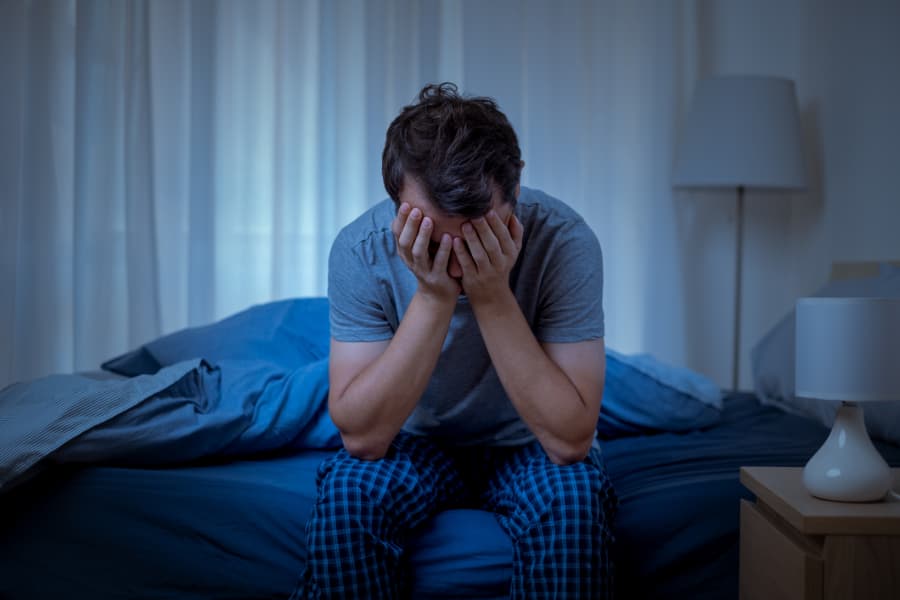 Person sitting in bed and covering face expressing discouragement