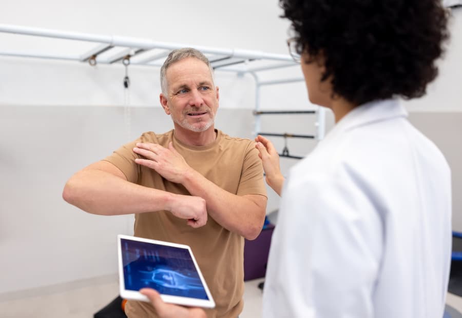 Patient discussing rotator cuff pain with orthopedist holding X-ray image 