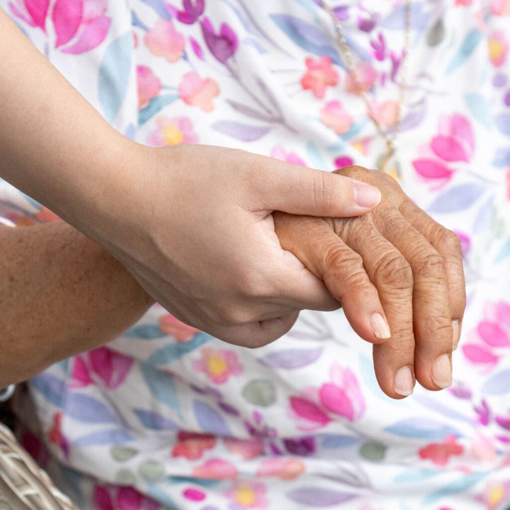 Elderly person in armchair holding hand of young caregiver