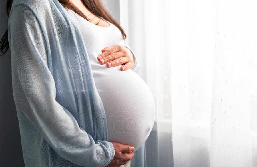 Side view of woman with advanced pregnancy standing by window